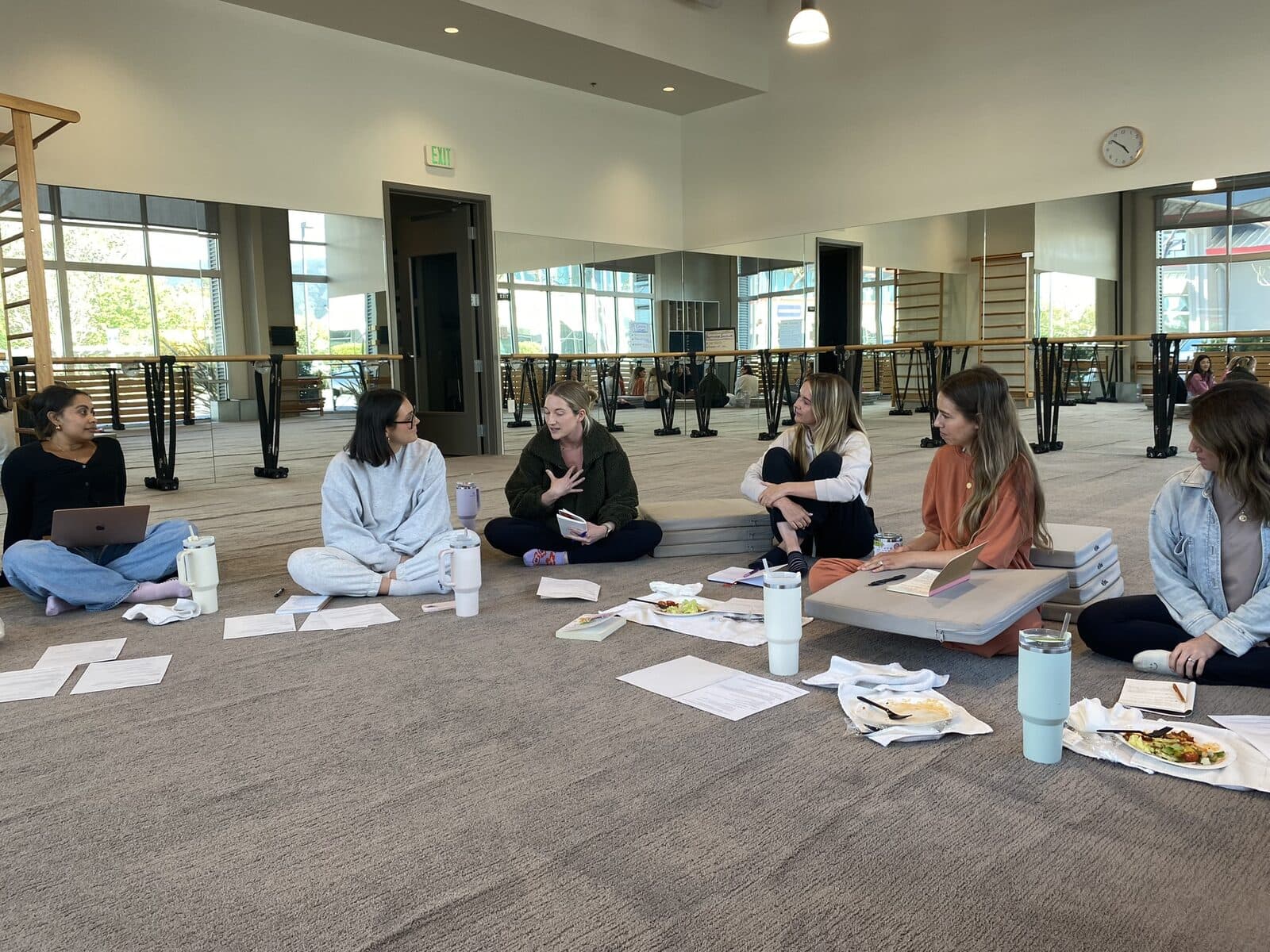 Women sitting in a circle on the studio floor, one speaking while the others listen