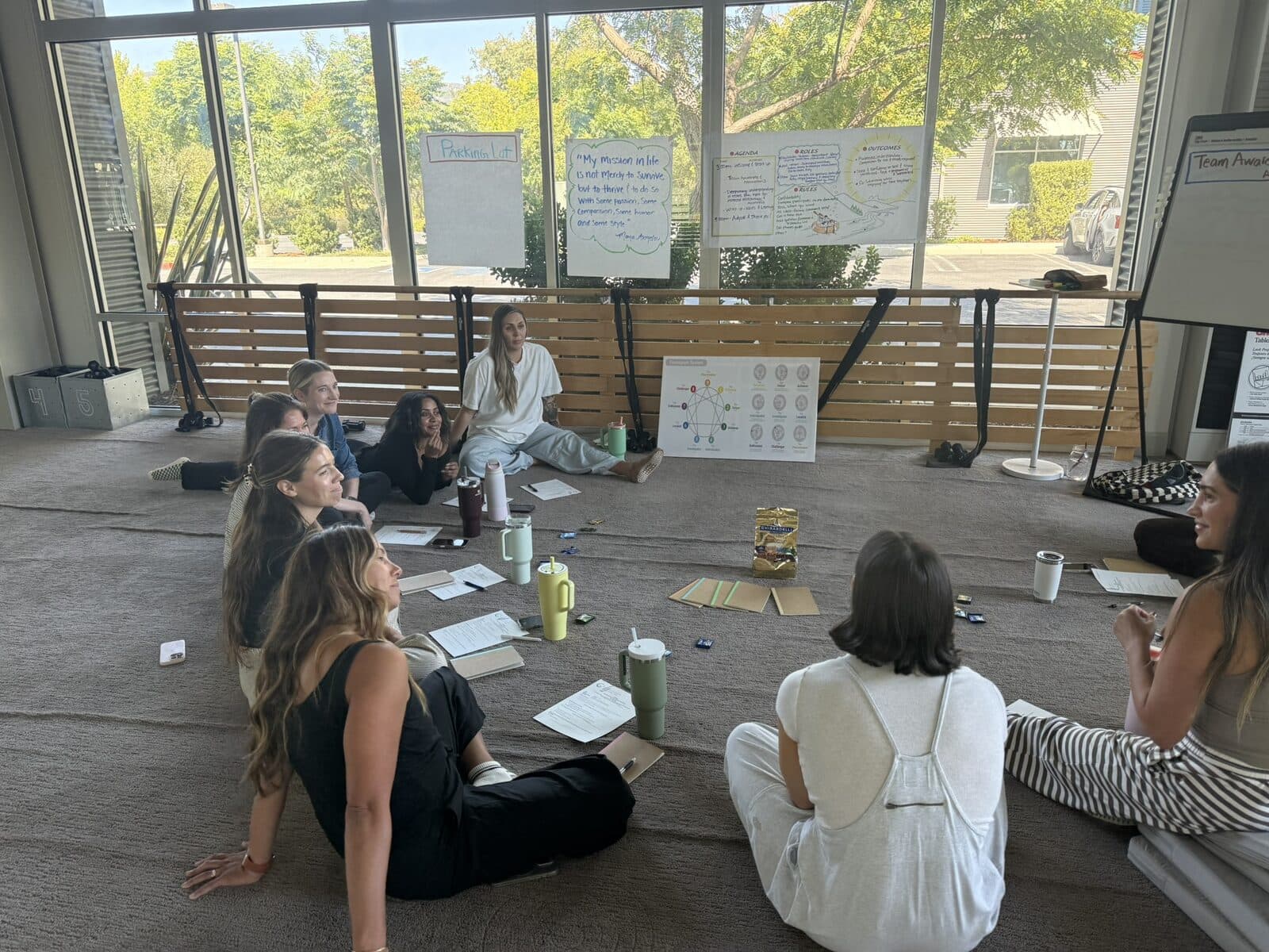 Workshop participants seated on the floor, looking at an Enneagram diagram and flip charts by a sunny window