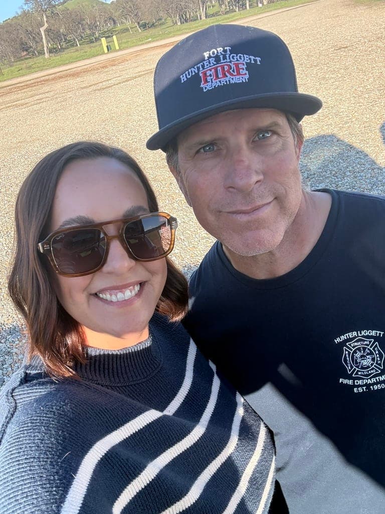 Katie in sunglasses and her husband in a Fort Hunter Liggett Fire Department cap, smiling together outdoors