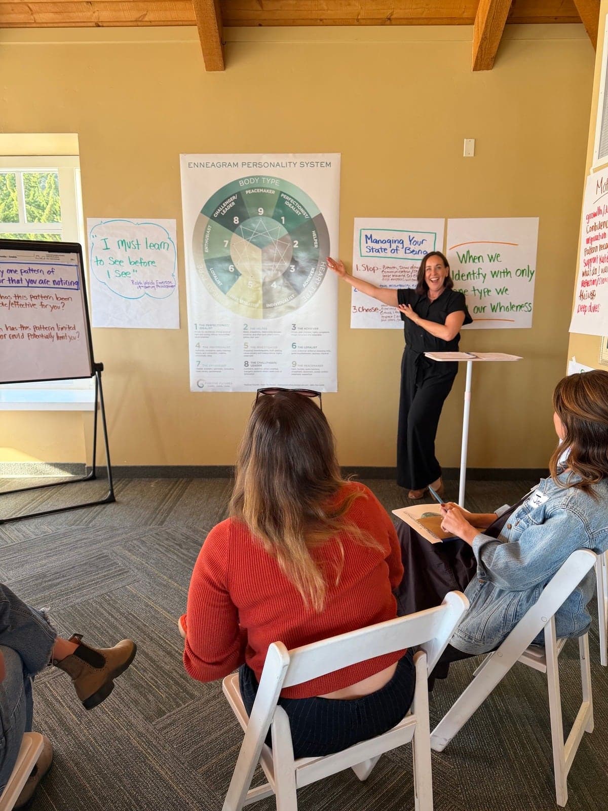 Katie pointing at a large Enneagram poster as she teaches, smiling at the room